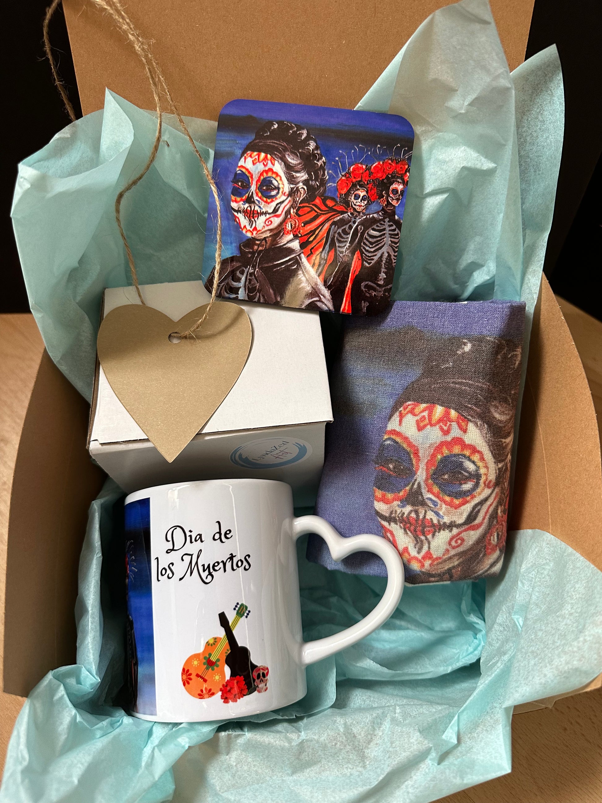 Mexican Girl Dia de los Muertos giftbox showing heart handle on mug, text and guitar graphic, coaster and folded tote bag